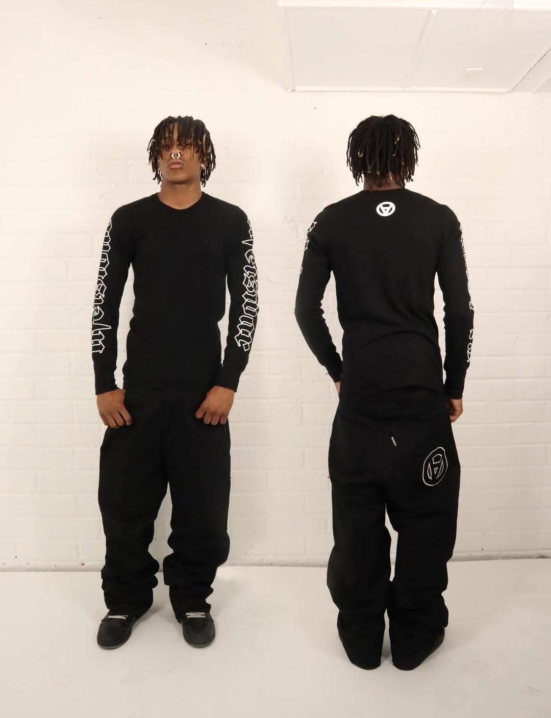 Person wearing a black outfit with white text and logos, standing against a white background.