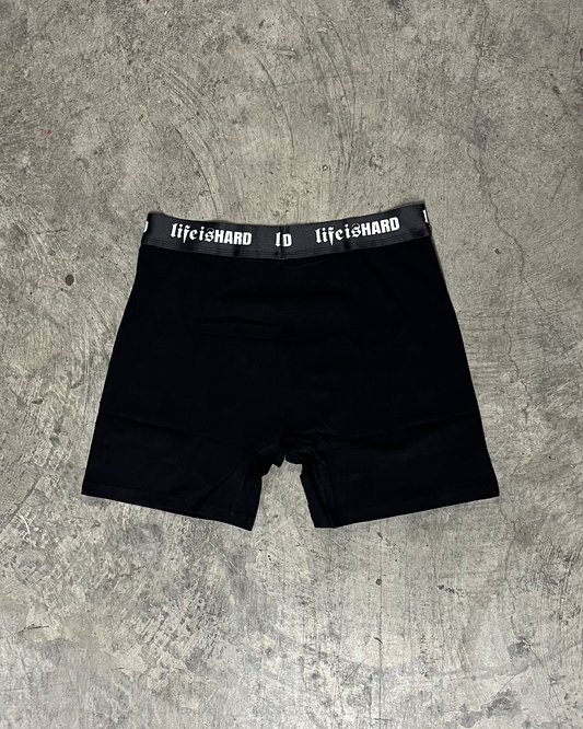 Black boxer briefs with 'lifetoshard' waistband on a gray concrete surface