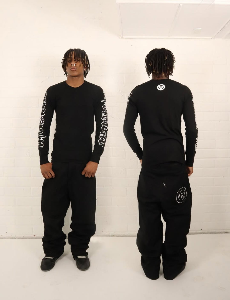 Person wearing a black outfit with white text and logos, standing against a white background.