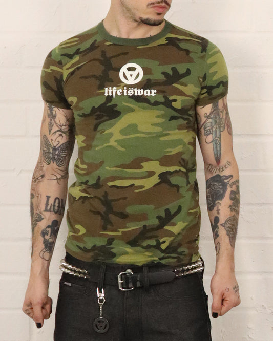 Person wearing a camouflage t-shirt with 'life is war' logo against a white brick wall.