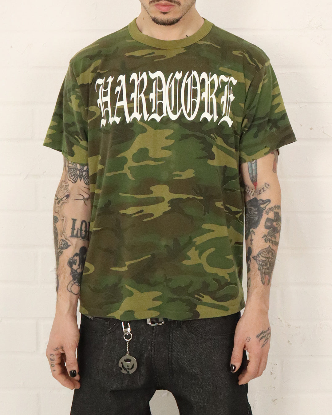 Person wearing a camouflage t-shirt with 'HARDCORE' text against a white background