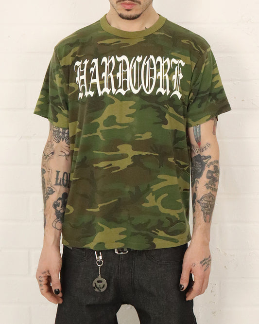 Person wearing a camouflage t-shirt with 'HARDCORE' text against a white background