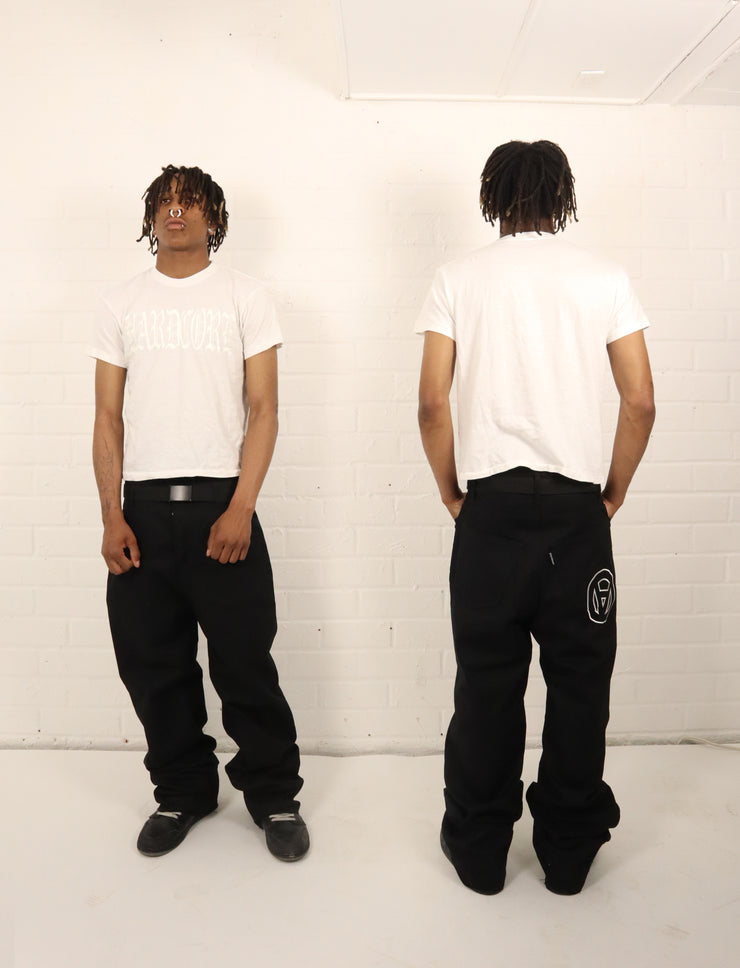 Person wearing a white t-shirt and black pants with a logo, standing against a white background.