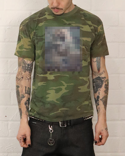 Person wearing a camouflage t-shirt with a blurred patch on a white brick wall background