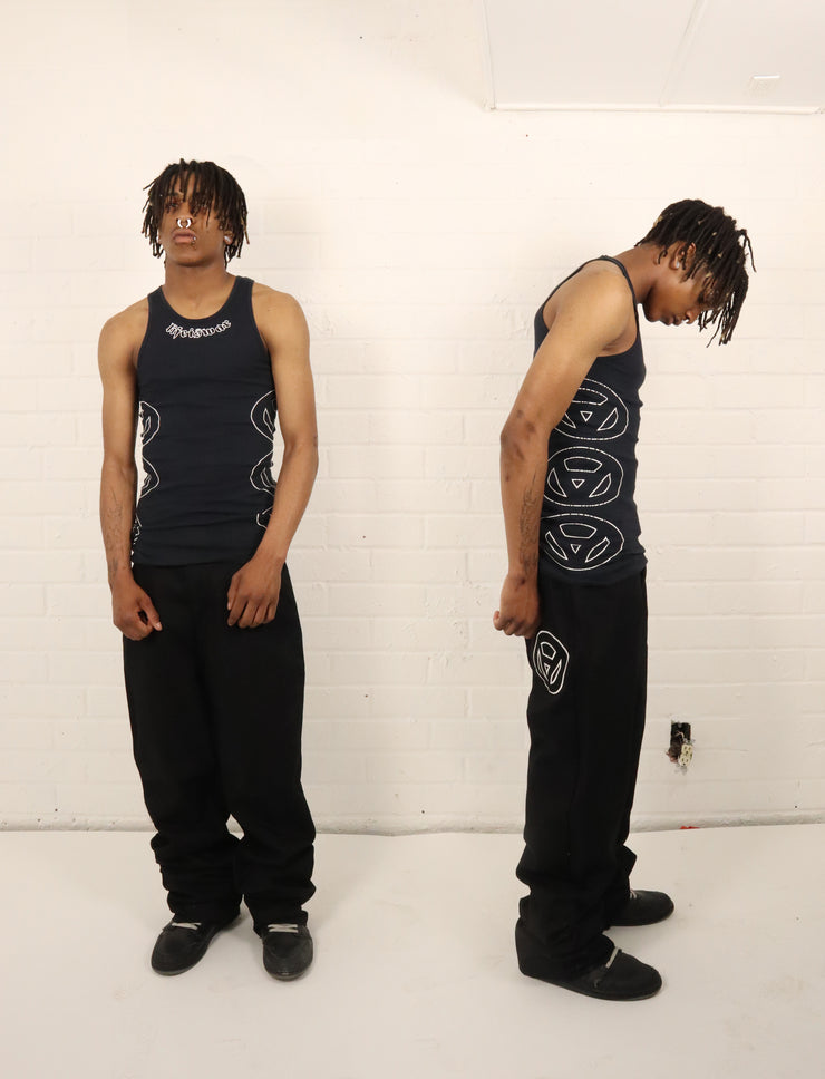 Two poses of a person wearing a black tank top with white graphics and black pants against a white wall.
